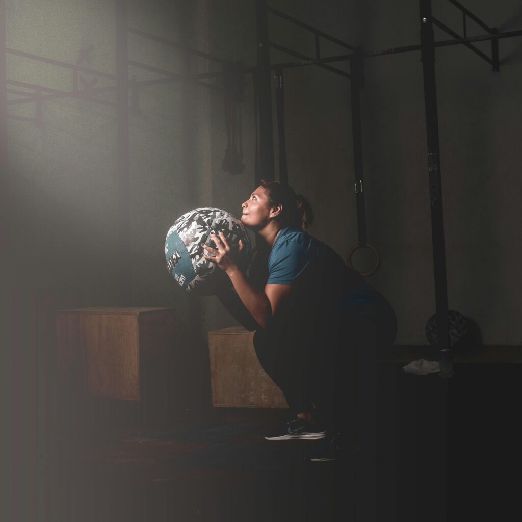 A woman performs a workout with a medicine ball in a dimly lit gym in Mérida, Mexico.